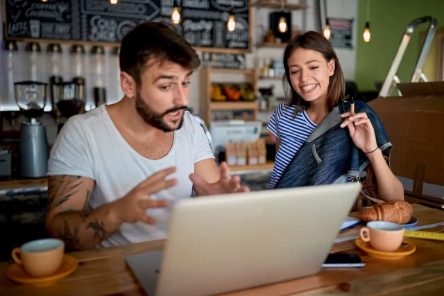 Excited business owner looking at his computer with his wife beside him smiling